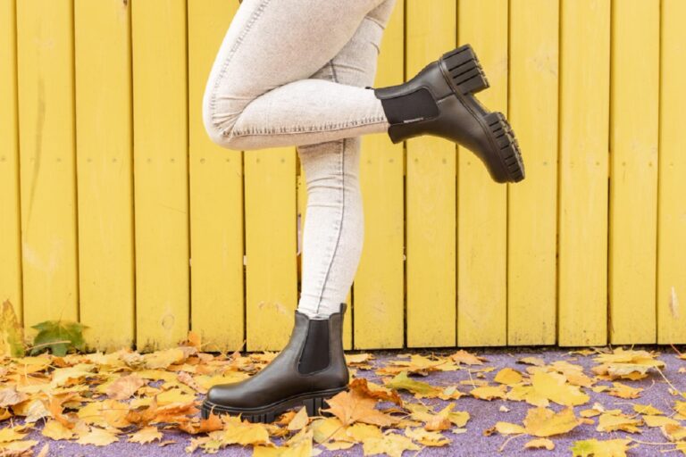 woman wearing black rain boots stands front yellow wooden wall 1